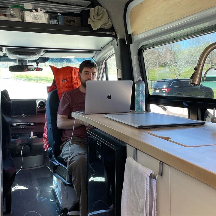 A man sitting in a chair in a van working on a laptop