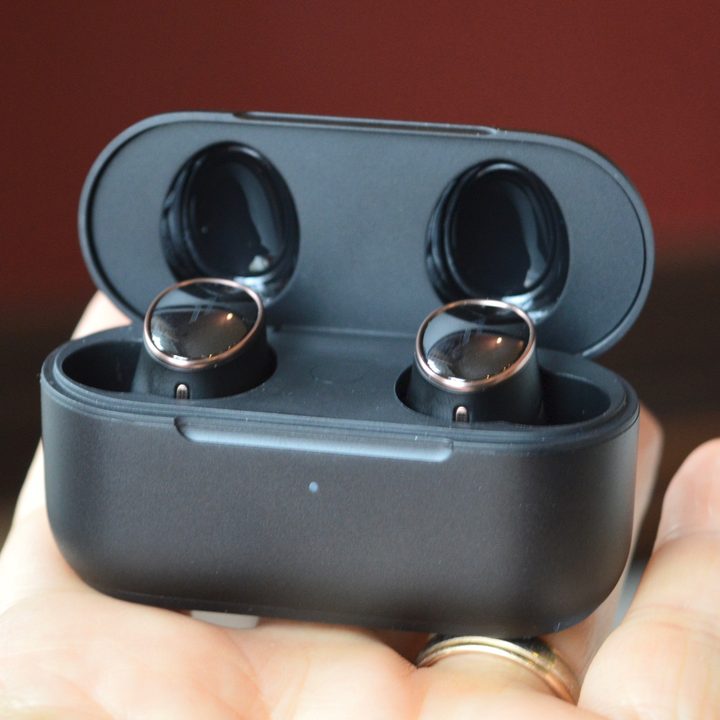 A hand holding the 1More Evo earbuds in their charging case.