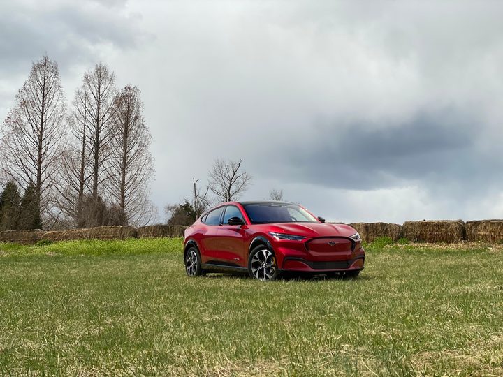 Angled front-end view of 2021 Ford Mustang Mach-E from passenger's side in a field.