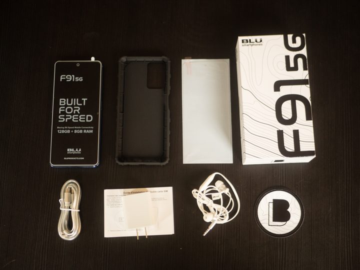 Contents from the Blu F91 5G smartphone laid out on a black wooden table