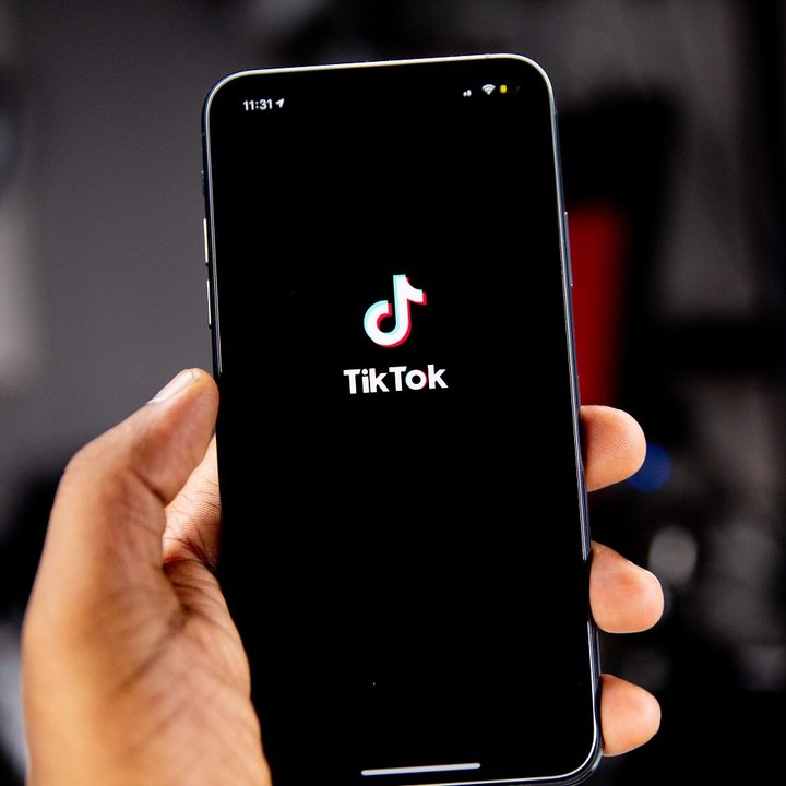 Person's hand holding a smartphone with TikTok's logo on screen, all in front of a blurred background.