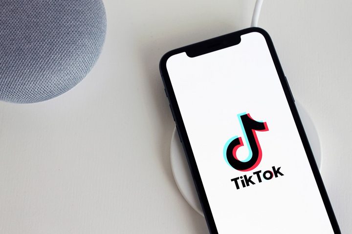 A smartphone and two other devices on a white table. The smartphone has the TikTok logo on its screen.