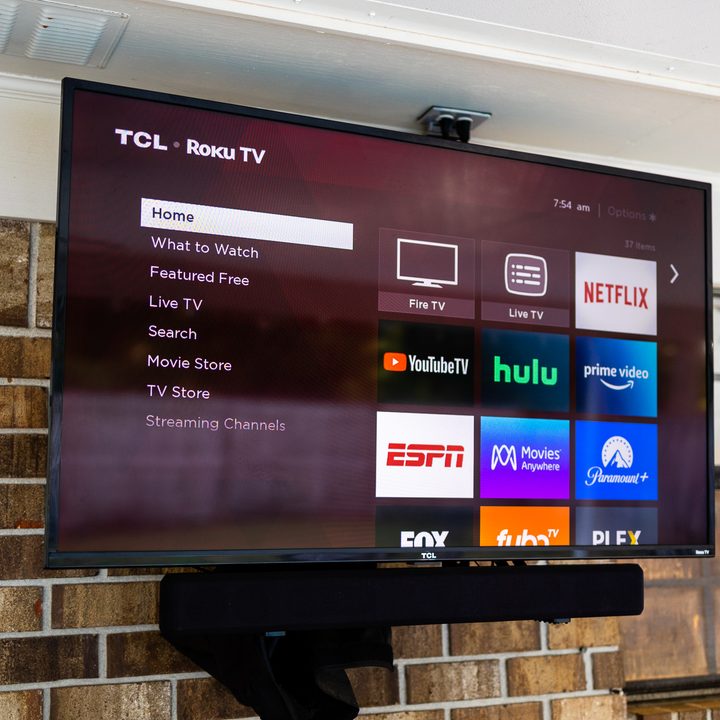 A TCL Roku TV and soundbar mounted to an outdoor wall.