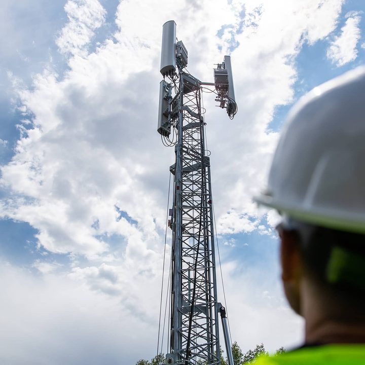 Worker looking up at 5G tower against a cloudy sky.