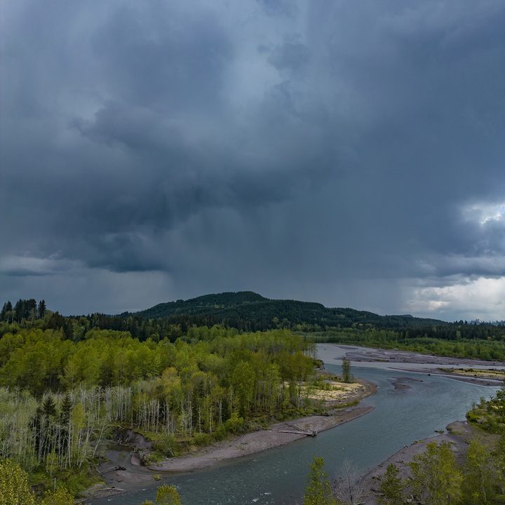 A river with a dark rainstorm over a mountain.