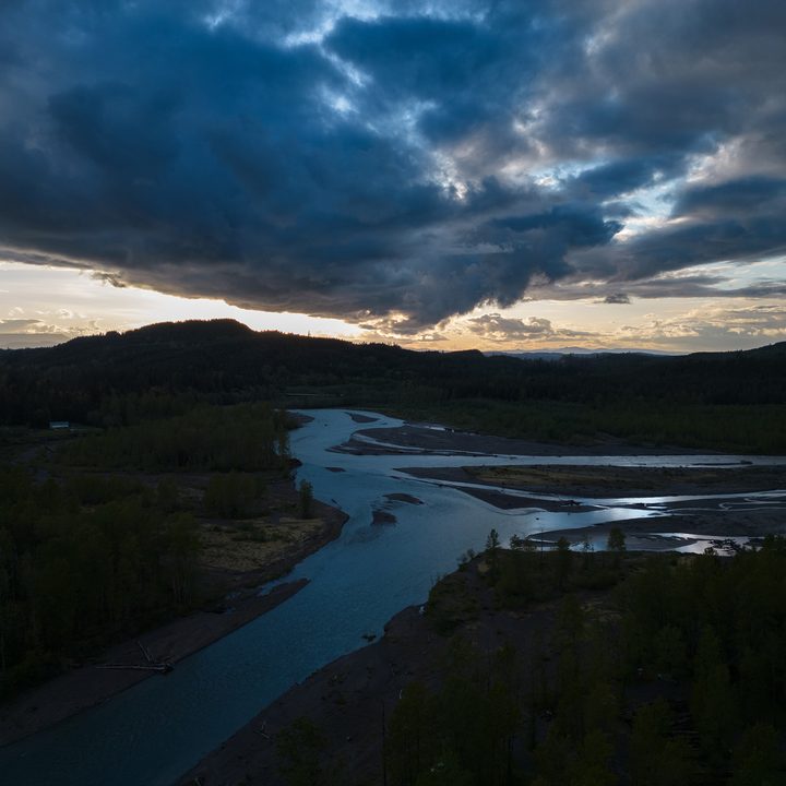 Sunset over a wild river shadowed by storm clouds.