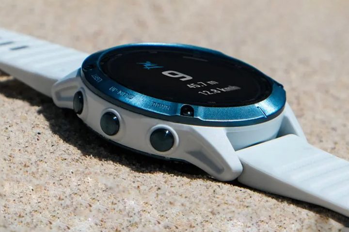 A Garmin Fenix 6 Pro Solar rests in the sand on a sunny day.