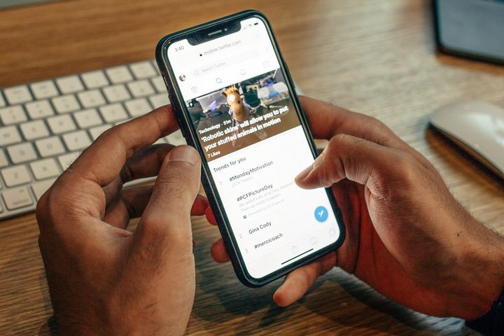 A person's hands holding a smartphone as they browse Twitter on it.