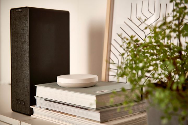 The new IKEA DIRIGERA hub sitting on books in front of a mirror next to a plant.