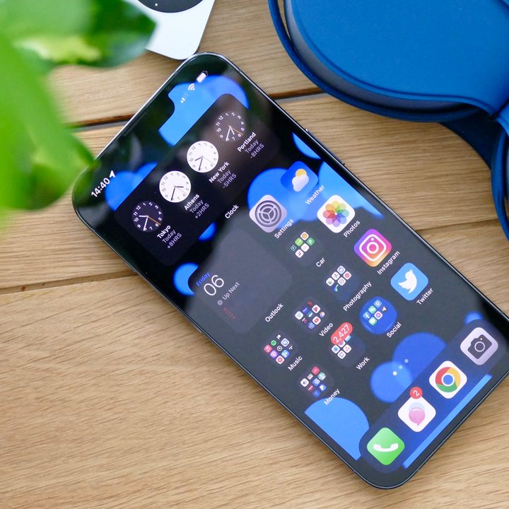 iOS Home screen shown on an iPhone 13 Pro, resting on a desk.