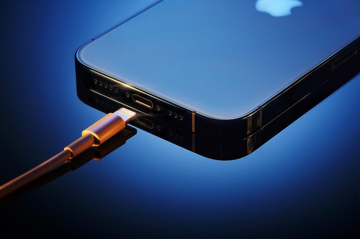 A blue iPhone 12 sits next to a lightning charger.