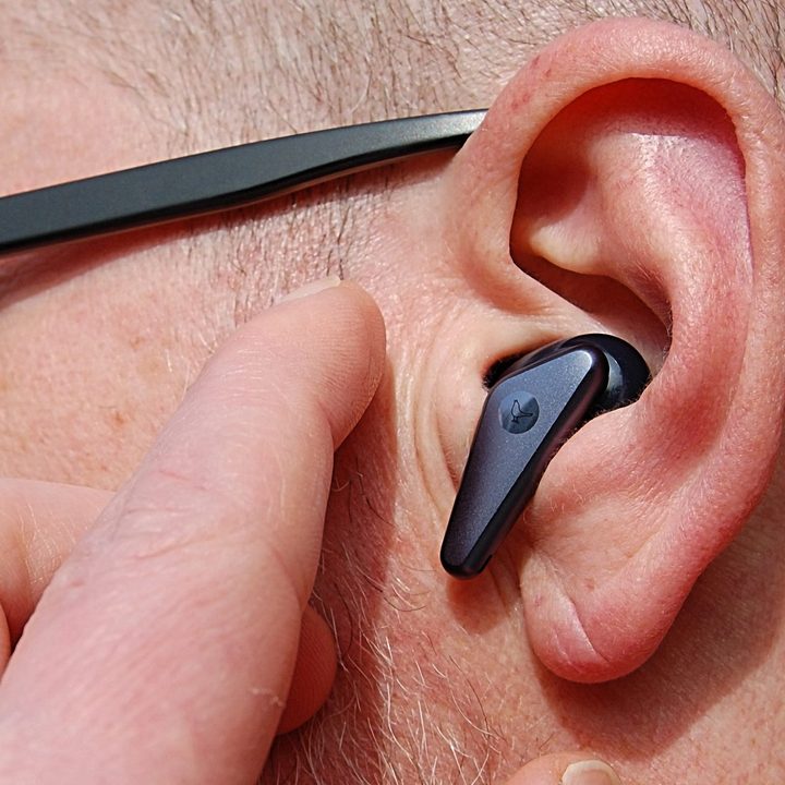 Wireless earbud in ear about to be tapped.