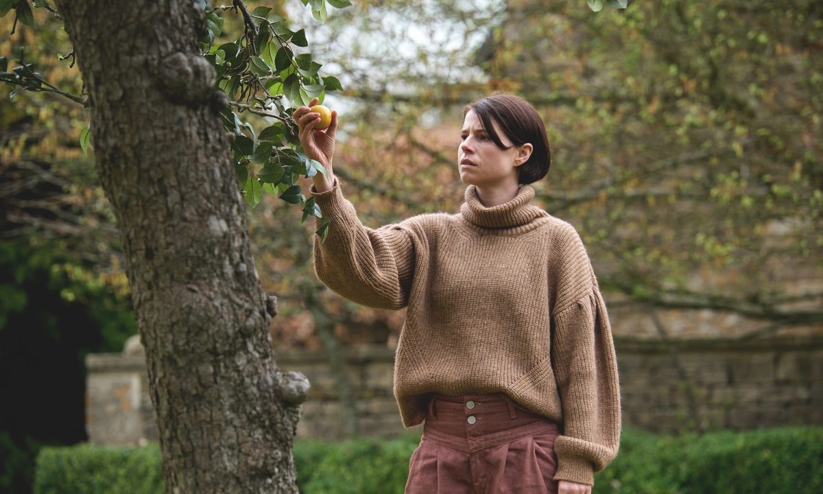 Jessie Buckley picks an apple from a tree in a scene from Men.
