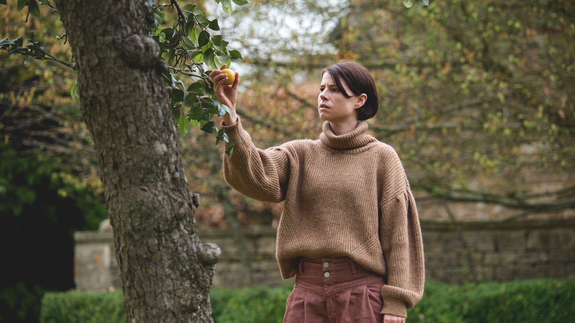 Jessie Buckley picks an apple from a tree in a scene from Men.