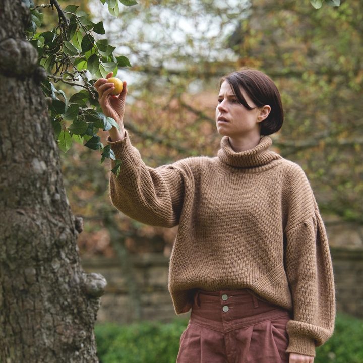 Jessie Buckley picks an apple from a tree in a scene from Men.