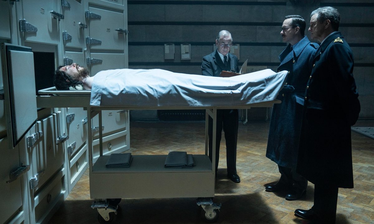 Two British officers stare at a corpse inside a morgue in a scene from Operation Mincemeat.