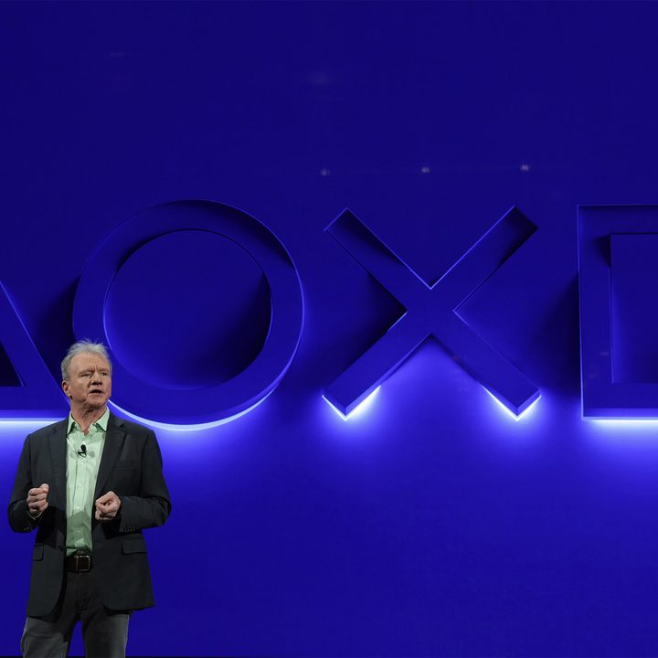 Playstation CEO and president, Jim Ryan, stands in front of a blue wall with Playstation button symbols illuminated.