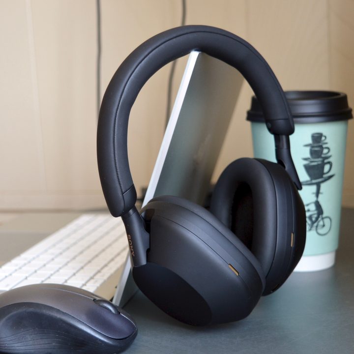 Sony WH-1000XM5 wireless headphones next to a laptop, mouse, and coffee cup.