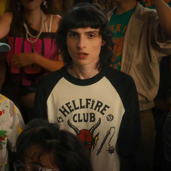 Gaten Matarazzo, Finn Wolfhard, and Sadie Sink stand in a crowd during a high-school rally in a scene from Stranger Things 4.