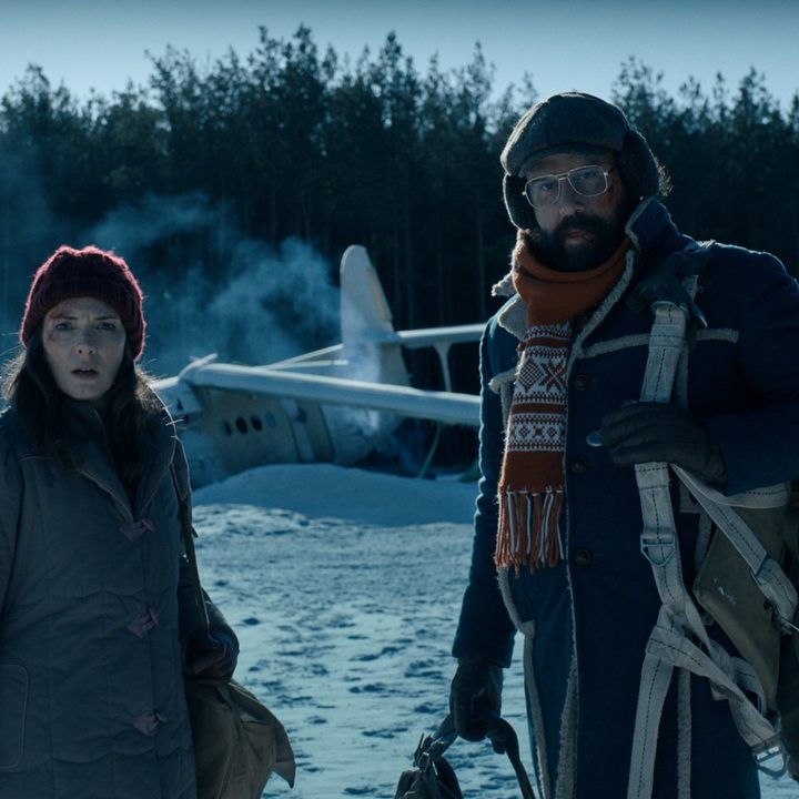 Winona Ryder and Brett Gelman stand in front of a crashed plane in the snow in a scene from Stranger Things 4.