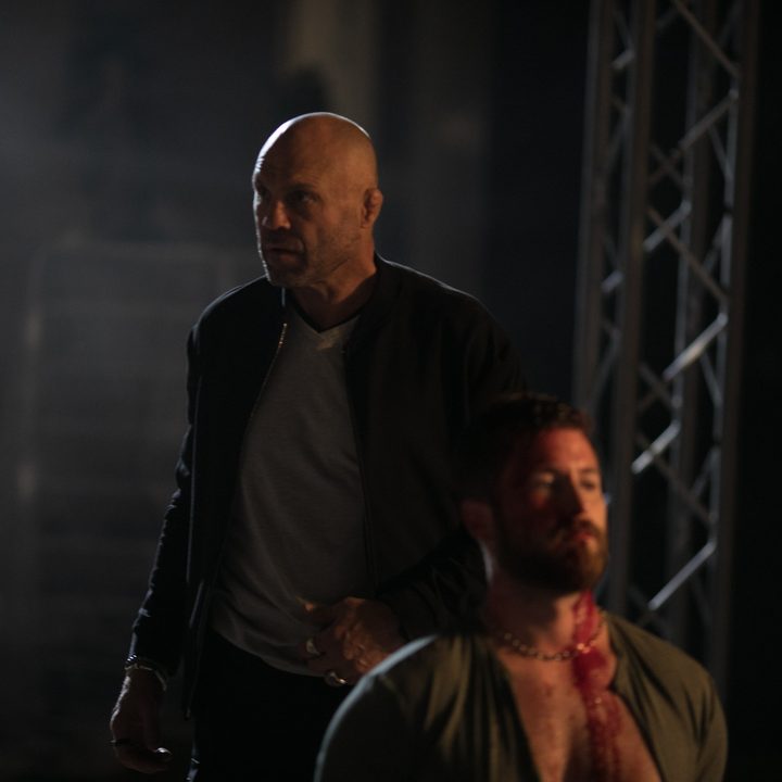 Randy Couture walking behind someone tied up in a scene from Blowback.