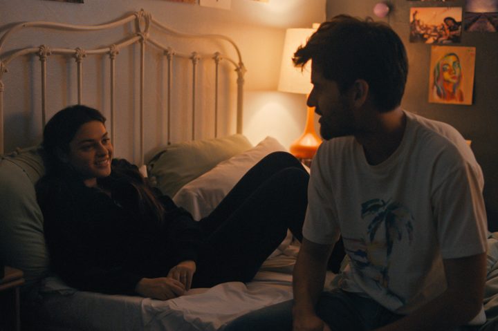 Andrew sits on a bed with Macy in Cha Cha Real Smooth.