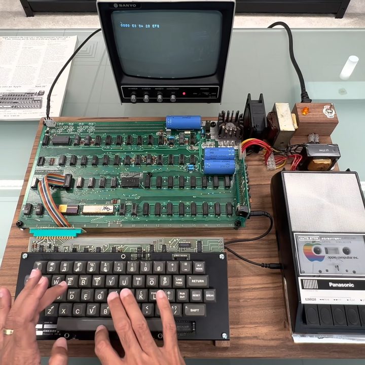 Apple-1 computer, sat on a table, with a person typing on its keyboard.