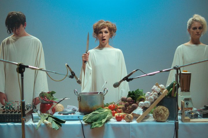 Billy, Elle, and Lamina stand in front of a banquet table together in Flux Gourmet.