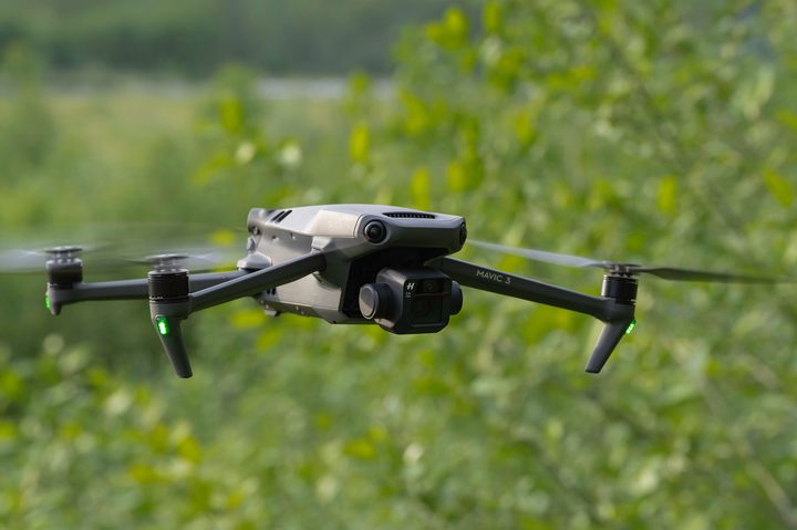 The DJI Mavic 3 in flight with trees in the background.