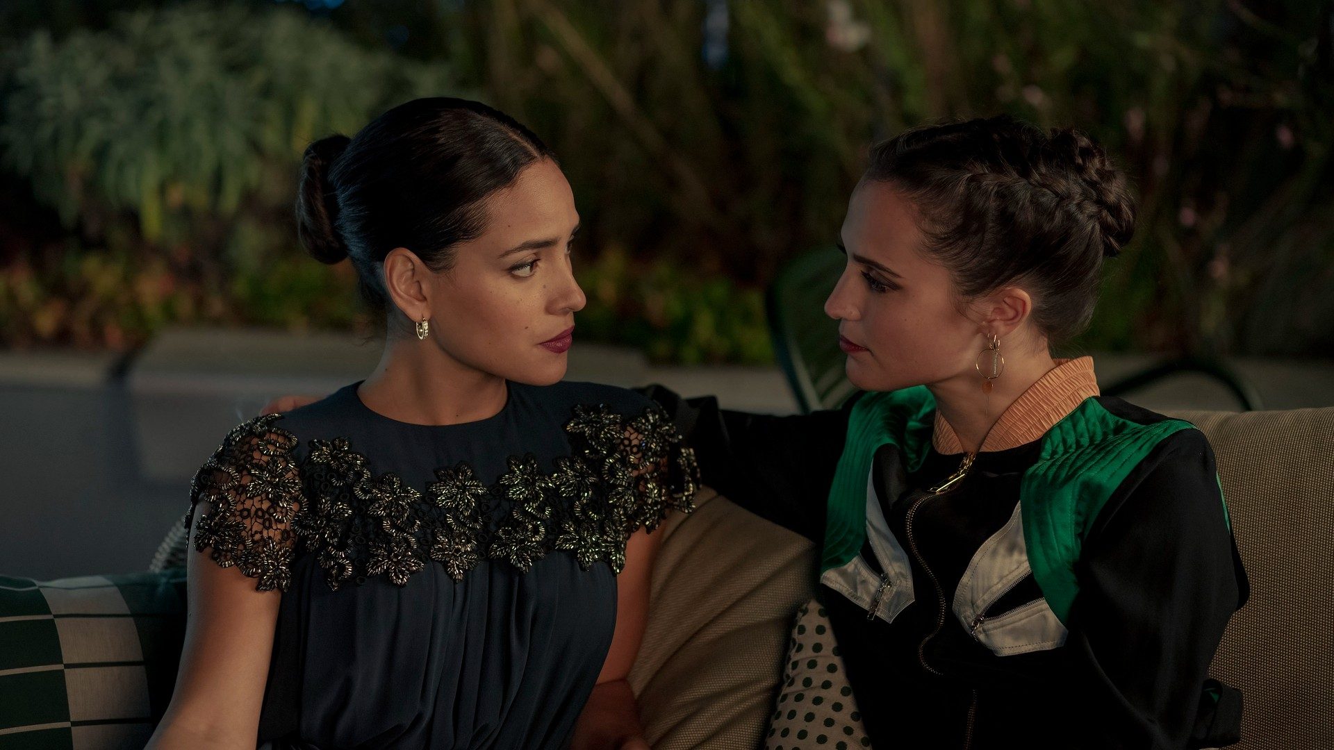 Adria Arjona and Alicia Vikander get close on a couch.