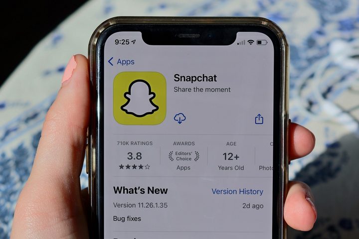 A hand holding a phone that shows app store listing for Snapchat app on its screen.