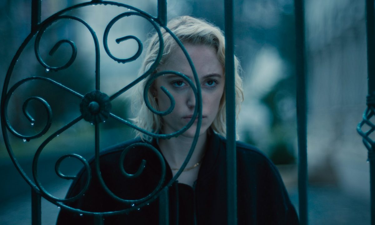 Maika Monroe stares through a gate in Watcher.