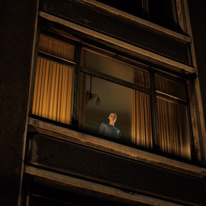 Maika Monroe peers out of a high window.