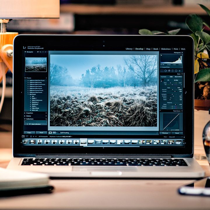 A Macbook sits on a desk with Adobe Lightroom opened on screen.