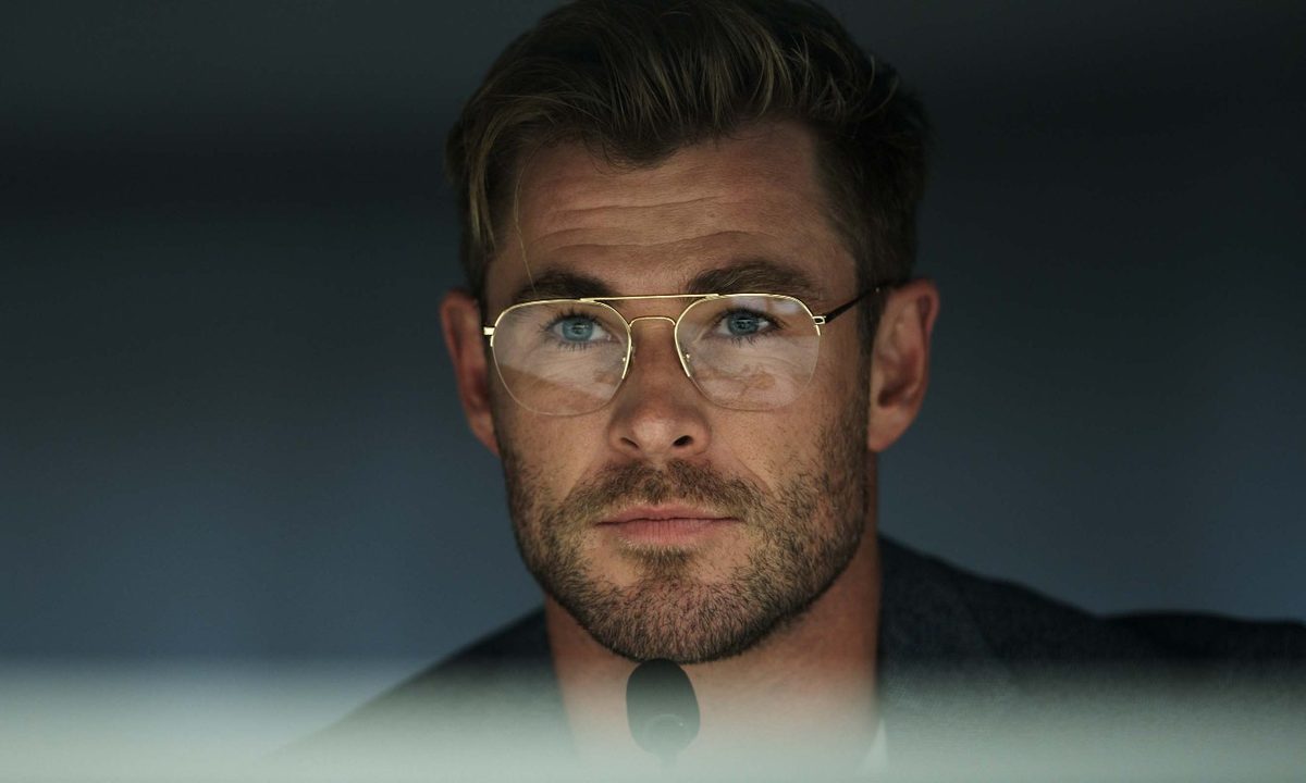 Chris Hemsworth smirks in front of a mi crophone in a scene from Spiderhead.