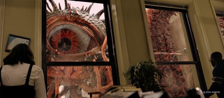 People look out a window in an office building with a giant eye and tentacles outside it in a scene from Doctor Strange in the Multiverse of Madness.