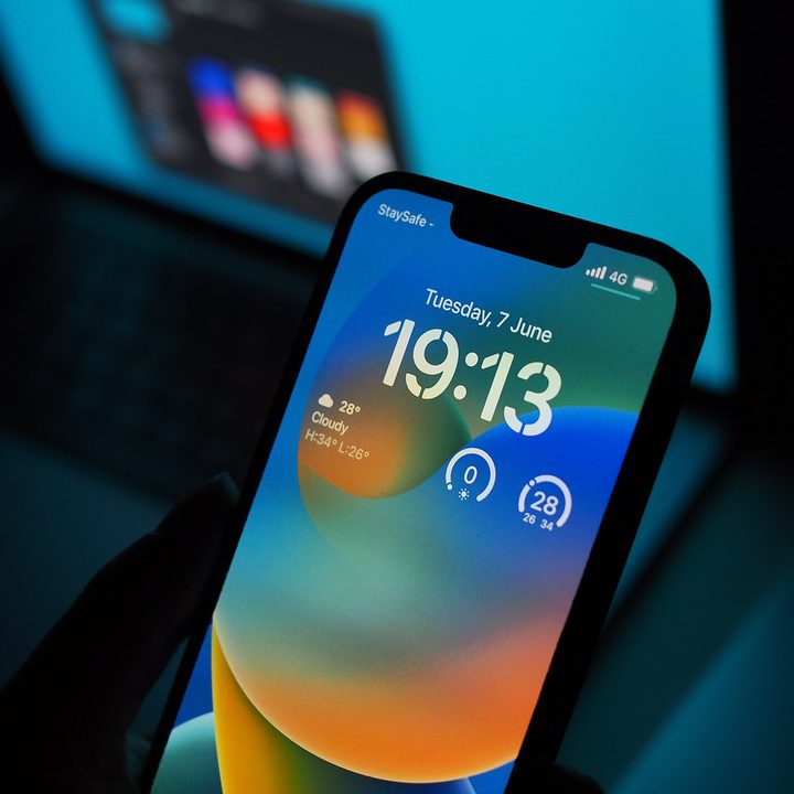 An iPhone 13 Pro running iOS 16 is held up in front of a Macbook.