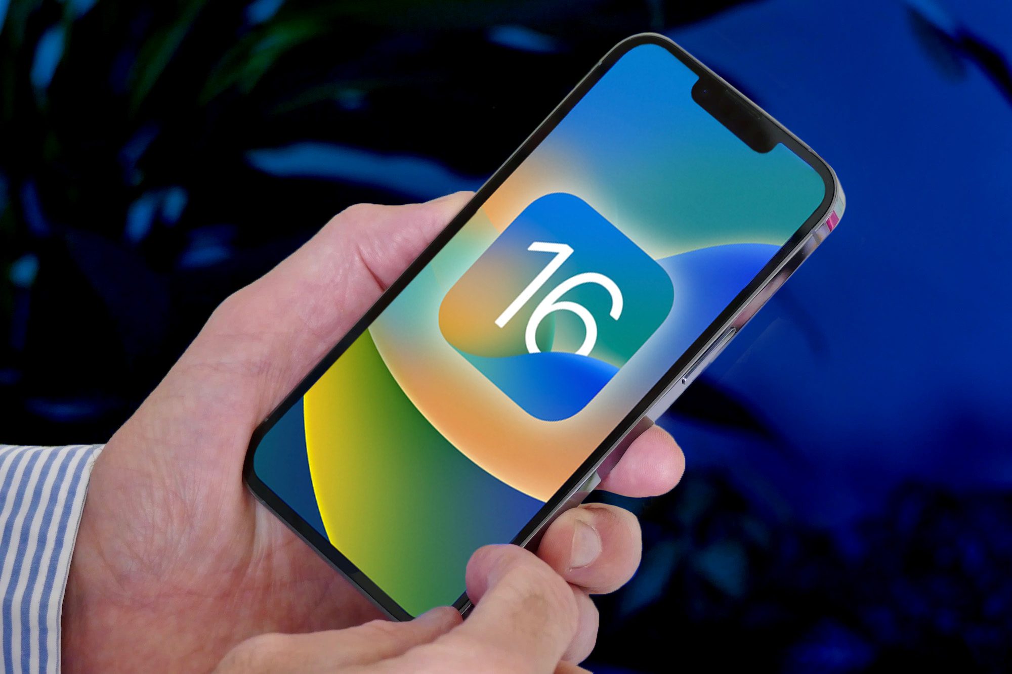 Man holds an iPhone 13 Pro with the iOS 16 logo on screen.