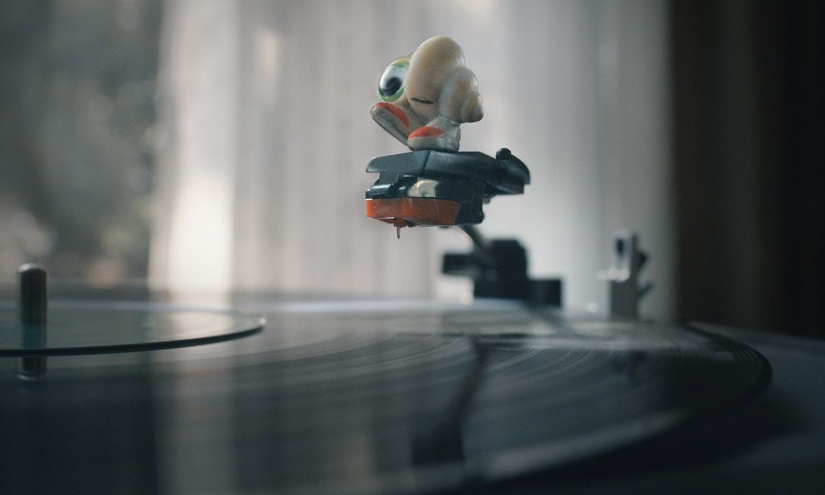 Marcel the Shell stands on the record player's needle, smiling.