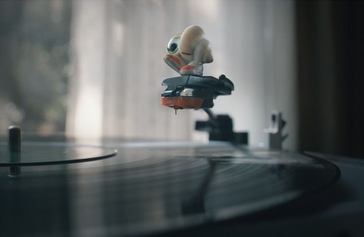 Marcel the Shell stands on the record player's needle, smiling.