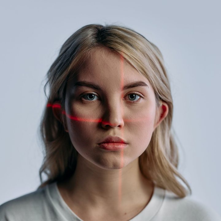 blonde woman with an expressionless face looks at camera while laser lights scan her features