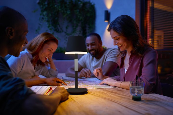 Philips Hue Go Lamp on a patio table where friends are sitting together at night.