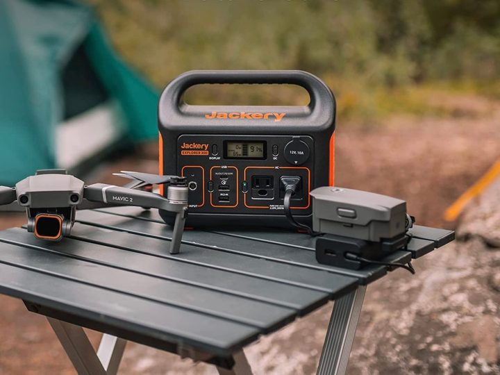 Jackery Portable Power Station Explorer 300 sits on a table at a camping site next to a drone.