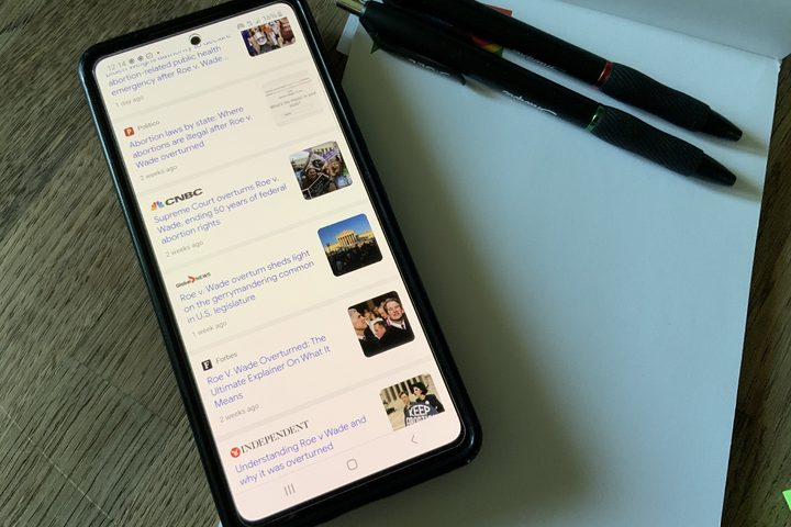 Articles of Roe vs. Wade overturned are visible on a phone screen overtop a notepad.