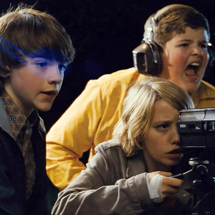The main characters from the sci-fi horror film "Super 8" filming something with a camera and screaming excitedly.