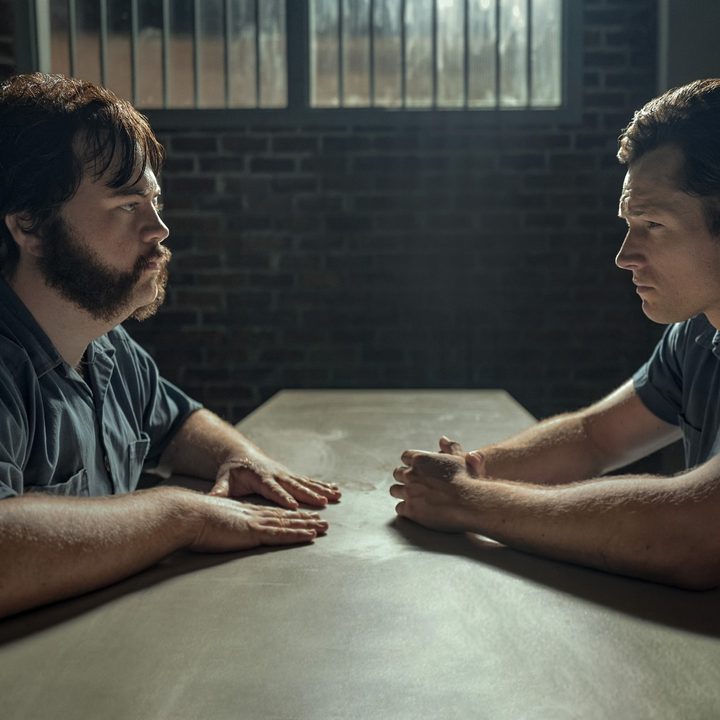 Paul Walter Hauser and Taron Egerton sit at a small table in prison, facing each other, in a scene from Black Bird.