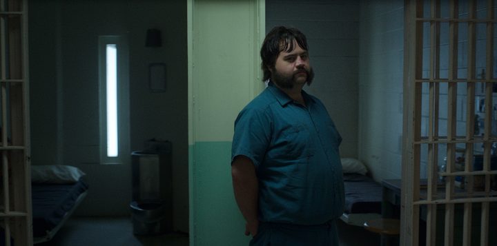 Paul Walter Hauser leans against the door of his character's prison cell in a scene from Black Bird.
