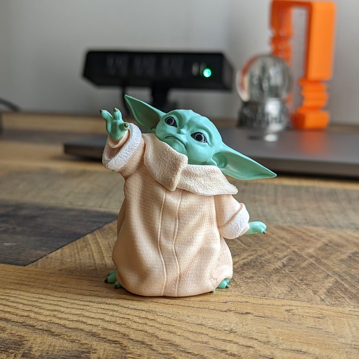 A photo of a small Grogu figurine standing on a desk.