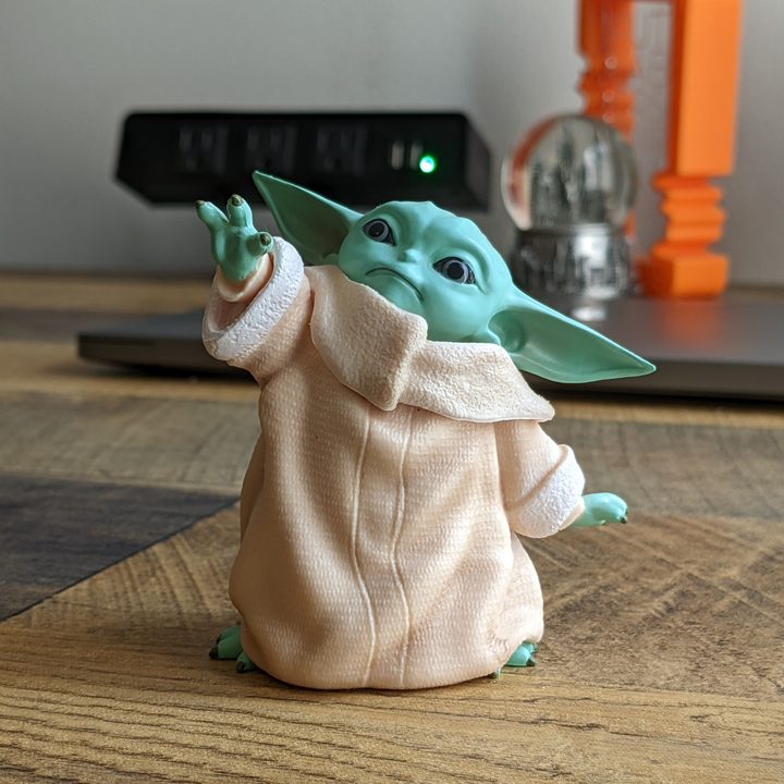 A photo of a small Grogu figurine standing on a desk.