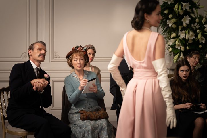 People look at a model posing in a pink dress in Mrs. Harris Goes to Paris.